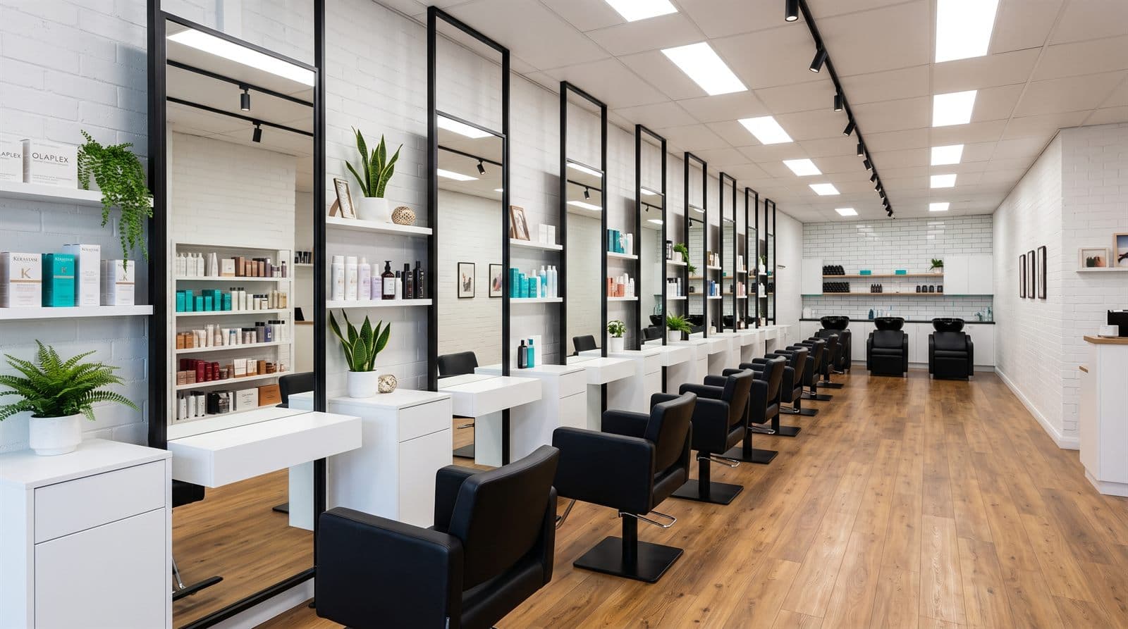 Salón de peluquería moderno y ordenado, con estaciones de trabajo alineadas, espejos verticales y sillones negros.
